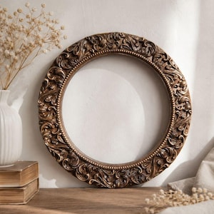 May include: A circular picture frame with a dark bronze finish and intricate, raised scrollwork and leaf patterns. The frame features a beaded inner border and a smooth, empty centre, showcasing a detailed relief design throughout the entire outer edge.