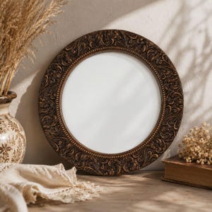 May include: A circular wall mirror featuring a dark brown frame with an intricate, raised relief scrollwork pattern. The mirror has a smooth, reflective centre surface and a beaded inner edge detail surrounding the glass, creating a textured appearance.