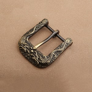 Puede incluir: Hebilla de cinturón de latón antiguo con diseño de dragón. La hebilla es cuadrada con esquinas redondeadas y presenta intrincados grabados de dragones en los bordes. La clavija es de un color latón más oscuro.