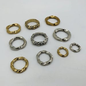 May include: Assortment of silver and gold metal rings, some with a twisted design and others with a decorative floral pattern.