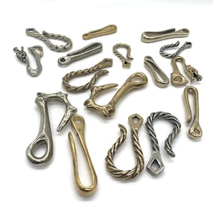 Könnte beinhalten: Eine Sammlung von 15 verschiedenen Schlüsselanhängern aus Metall in Silber- und Goldtönen. Die Schlüsselanhänger haben verschiedene Designs, darunter Seil, Haken und abstrakte Formen.