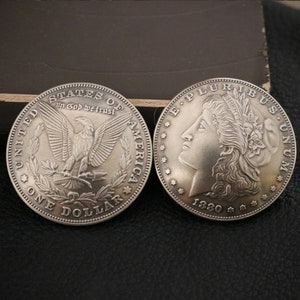 Puede incluir: Dos monedas de un dólar de plata, una con un águila calva y las palabras "United States of America" y "In God We Trust", la otra con un perfil de mujer y las palabras "E Pluribus Unum" y "Liberty".