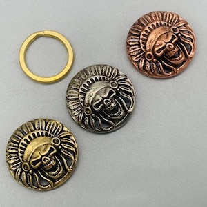 Puede incluir: Tres botones de metal con una calavera que lleva un tocado. Los botones son de oro, plata y cobre.