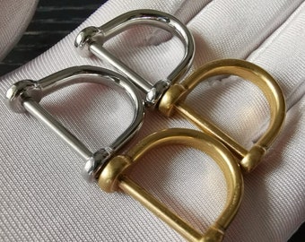 May include: Two metal D-rings, one silver and one gold, are shown on a white fabric surface. The rings are connected together.