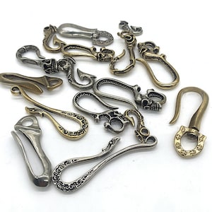 Könnte beinhalten: Eine Sammlung von 14 silbernen und goldenen Schlüsselanhängern mit filigranen Designs. Die Schlüsselanhänger haben verschiedene Formen, darunter Haken, Schlaufen und Schädel.