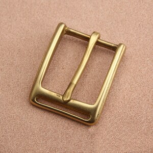 May include: A brass belt buckle with a rectangular shape and a smooth, polished finish.