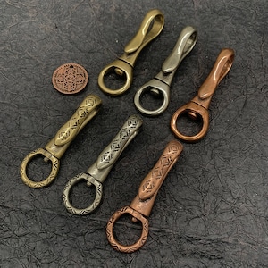 以下が含まれることがあります： 装飾的なデザインが施された金属製のキーホルダーが6個あります。キーホルダーは、シルバー、ゴールド、銅など、さまざまな色があります。各キーホルダーには、上部に小さなリング、下部にフックが付いています。