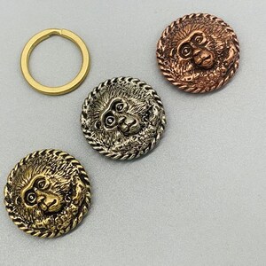 May include: Three round metal buttons featuring a monkey face design. The buttons are in gold, silver, and copper.