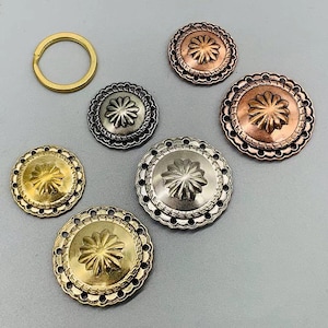 Op de afbeelding: Vijf decoratieve metalen knopen met een bloemmotief. De knopen zijn in verschillende kleuren, waaronder goud, zilver en koper.