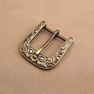 Puede incluir: Una hebilla de cinturón de metal dorado con un diseño floral adornado.