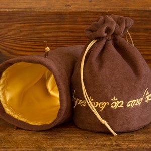 May include: Two brown velvet pouches with gold drawstring closures. One pouch has a gold satin lining and the other has the inscription "One Ring to rule them all, One Ring to find them, One Ring to bring them all and in the darkness bind them" embroidered in gold thread.