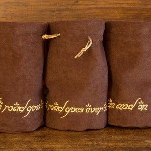 May include: Three brown fabric pouches with drawstrings. Each pouch has gold embroidery that reads "The road goes ever on and on".