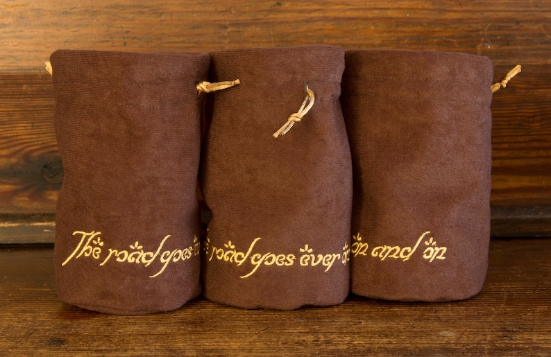 May include: Three brown fabric pouches with drawstrings. Each pouch has gold embroidery that reads "The road goes ever on and on".