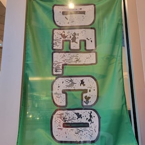 Peut inclure: Un drapeau vert avec le mot "DELCO" imprimé en blanc avec un aspect vieilli et délabré.