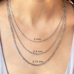 May include: Three silver chain necklaces of different widths, 2 mm, 2.4 mm, and 3.15 mm, are layered on a person's neck. The chains are all the same style, with a flat, oval-shaped link.