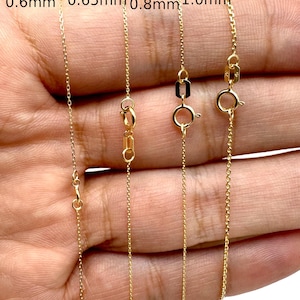 May include: Four gold cable chains with varying thicknesses labeled 0.6mm, 0.65mm, 0.8mm, and 1.0mm. Each chain features a circular spring ring clasp and a small rectangular tag near the closure, showcasing the different link sizes side by side.