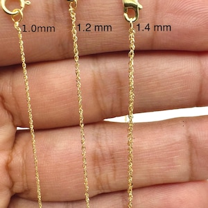 May include: Close-up of three gold-colored chain necklaces with different thicknesses: 1.0mm, 1.2 mm, and 1.4 mm. Each chain is shown with its clasp. The chains are displayed against a skin-toned background.