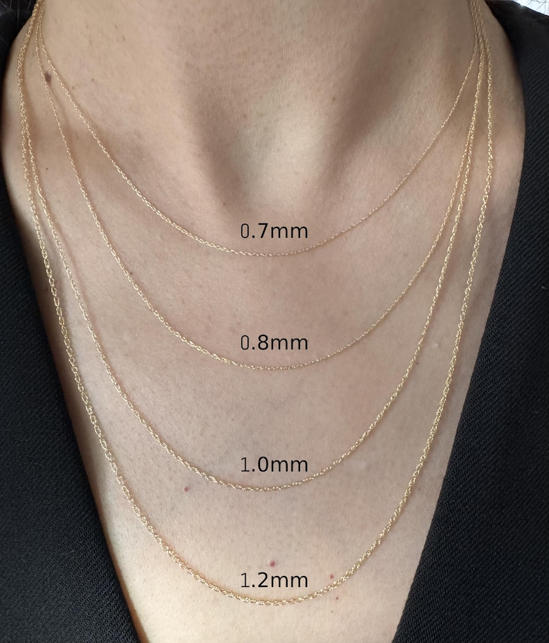 Może przedstawiać: Cztery złote łańcuszki o splocie typu cable ułożone warstwowo na szyi, każdy o innej grubości oznaczonej jako 0.7mm, 0.8mm, 1.0mm i 1.2mm. Łańcuszki charakteryzują się delikatnym, splecionym wzorem ogniw, co nadaje im jednolity, lśniący wygląd.