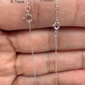 May include: Close-up of two silver chain necklaces, one 0.7mm and the other 1.0mm thick. Each chain has a spring ring clasp. The chains are displayed against a neutral background.