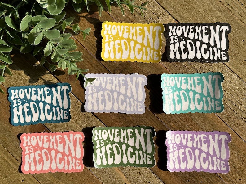 May include: A selection of stickers displaying the text "Movement is Medicine" in a retro style. The stickers are in a range of colours: yellow, black, teal, lavender, pink, green, and purple. They are arranged on a wooden surface.
