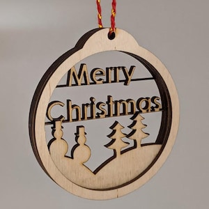 May include: A wooden Christmas ornament with the words "Merry Christmas" cut out. The ornament features a snowman and Christmas tree design. It hangs from a red and gold string.