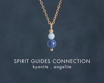 May include: A gold chain necklace featuring a pendant with a small light blue bead and a larger dark blue bead. The text SPIRIT GUIDES CONNECTION kyanite . angelite and CRYSTALLIUM is printed below the pendant on a dark blue background.