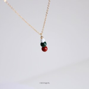 Pu&ograve; includere: Una delicata collana d'oro con un ciondolo composto da quattro perline colorate: rosse, verdi, bianche e dorate. Le perline sono infilate insieme, creando un design semplice ma elegante. La collana &egrave; esposta su uno sfondo morbido e neutro.