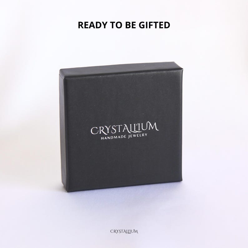 Pu&ograve; includere: Una scatola regalo quadrata nera con la scritta "READY TO BE GIFTED" in alto. La scatola ha il marchio "CRYSTALLIUM" e le parole "HANDMADE JEWELRY" stampate in bianco. Il marchio &egrave; stampato anche in basso.