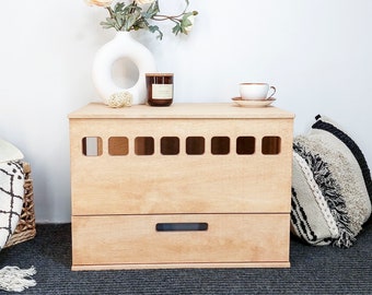 May include: A rectangular light-toned wooden storage chest featuring a row of eight square cut-out ventilation holes along the upper section and a single horizontal drawer below with a centered rectangular handle slot for easy opening.