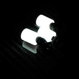 May include: Three glowing white cylindrical objects are clustered together against a dark background. The objects appear to be illuminated, with a textured surface visible in the lower part of the image.