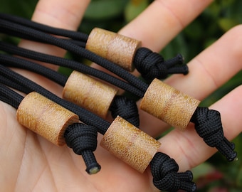 May include: Close-up of several black cords with cylindrical wooden beads. The beads have a light brown, textured surface. The cords are knotted at the ends.