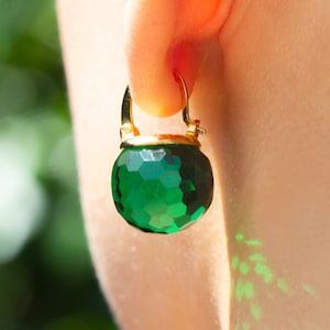 May include: Gold hoop earrings with a large, faceted, green gemstone.