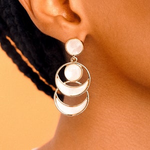 May include: Gold earrings with a white, layered, moon-shaped design.