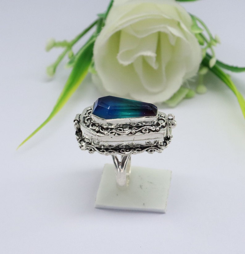K&ouml;nnte beinhalten: Ein silberner Ring mit einem Sargf&ouml;rmigen blauen und gr&uuml;nen Edelstein. Der Ring ist mit kunstvollen silbernen Schn&ouml;rkeln verziert und hat einen Klappdeckel.