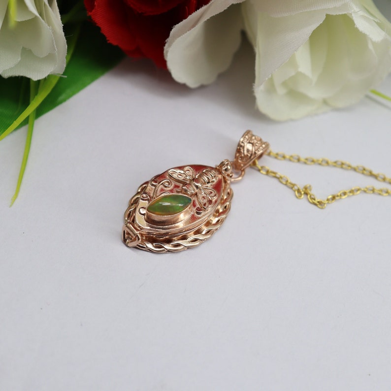 May include: A gold-toned pendant necklace with a green opal stone and a bee design. The pendant is oval-shaped and has a detailed, intricate design.