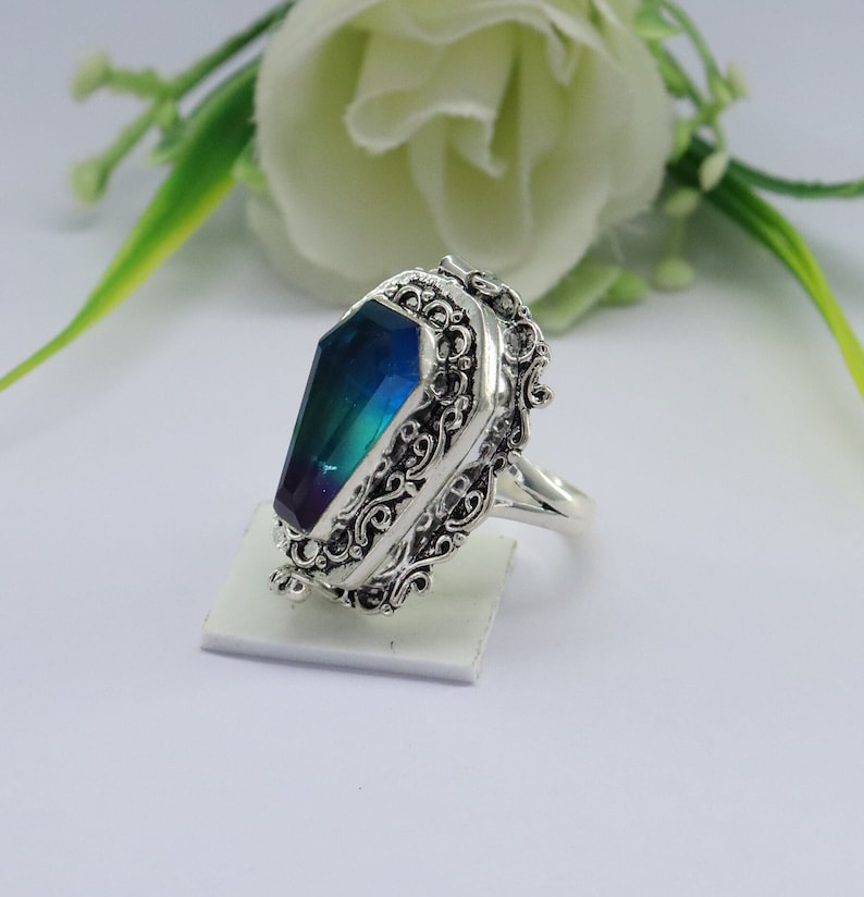K&ouml;nnte beinhalten: Ein silberner Ring mit einem blauen und gr&uuml;nen Edelstein, der in einem Sarg-Design gefasst ist. Der Ring hat komplizierte Filigrandetails.