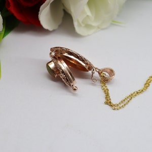May include: A gold locket necklace with a green stone and a detailed design. The locket is open, revealing an empty interior.