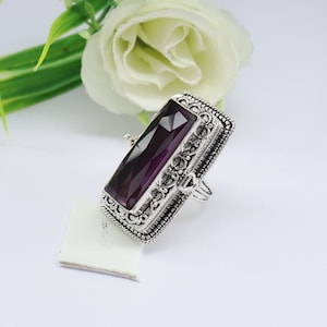 Può includere: Un anello d'argento con un designo ornato e una grande pietra preziosa rettangolare di colore viola.