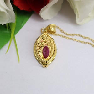 May include: A gold pendant necklace featuring a red gemstone set within an intricate floral design.