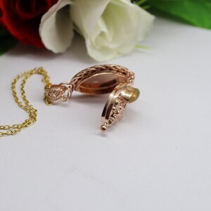 May include: A rose gold locket necklace with a delicate chain and a green opal stone. The locket is open, revealing an empty space inside.
