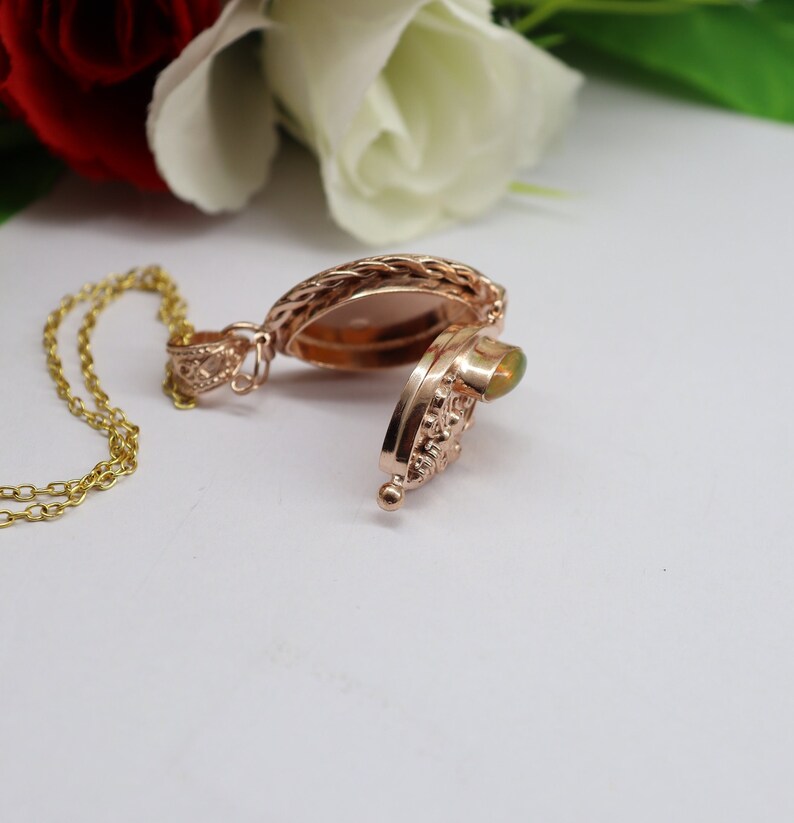 May include: A rose gold locket necklace with a delicate chain and a green opal stone. The locket is open, revealing an empty space inside.
