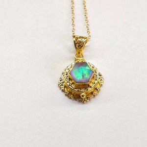 Puede incluir: Un collar de oro con un colgante que presenta una piedra preciosa hexagonal iridiscente rodeada de un marco de oro adornado.