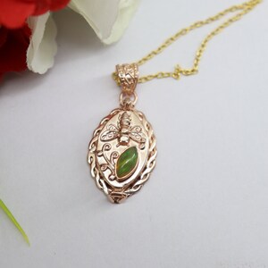 May include: A gold pendant necklace with a green opal and a bee design. The pendant is oval shaped and has a detailed design.