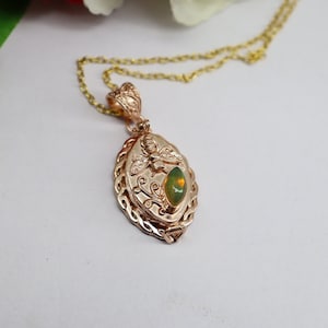 May include: A gold necklace with a pendant featuring a green opal stone and a bee design. The pendant is surrounded by a decorative, braided border.