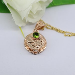 May include: A gold pendant necklace with a round charm featuring a green gemstone and a detailed design. The chain is gold.