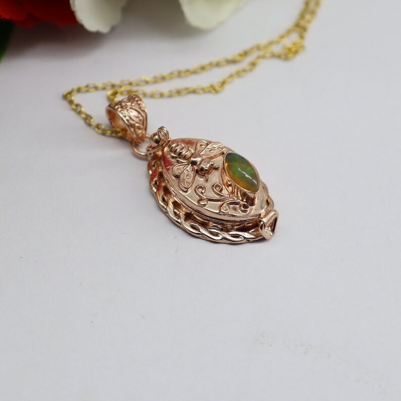 May include: A gold-tone necklace with a pendant featuring a green opal stone and a bee design. The pendant is oval-shaped and has a detailed floral pattern.