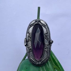 Könnte beinhalten: Ein silberner Ring mit einem verzierten Design und einem großen, facettierten, violetten Edelstein.