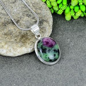 May include: A silver chain necklace with a pendant featuring a green, pink, and black oval gemstone.