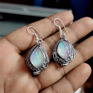 Peut inclure: Une paire de boucles d'oreilles pendantes en argent avec des gouttes de pierres précieuses irisées. Les boucles d'oreilles ont un design filigrané détaillé.