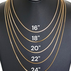 May include: Five gold chains of different lengths on a black display stand. The chains are labeled 16", 18", 20", 22", and 24".
